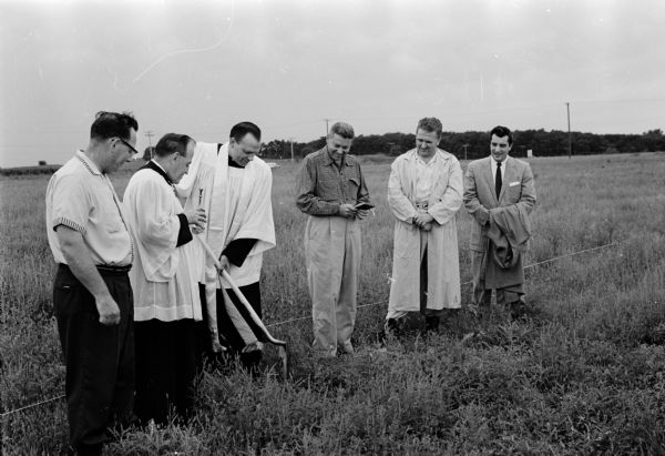 A group gathering for the ground breaking ceremonies for the St. Thomas Aquinas parish auditorium. Rev. Arnold Lehman, pastor, shown with shovel; sacristan Mathew Statz holding a vessel of holy water. Others, left to right:  E. H. Petterle, Thomas Gately, Russell Pavlat, and Joseph Oesterle.