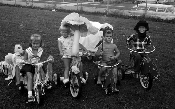 Four children pose on their tricycles during the Eastmorland bike parade. One of them is pulling a wagon designed to look like a pioneer covered wagon. Children include, left to right: Julie Phillips, Paula Holmen, and Pat and Dennis Kilbane.