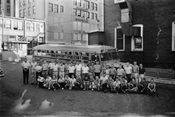 Group portrait of about 200 newspaper carrier boys posed in front of a school bus for the Madison Newspaper, Inc. Chosen for attributes such as promptness, courtesy and keeping their pick-up corner clean, they will be going to the State Fair in West Allis as a reward.