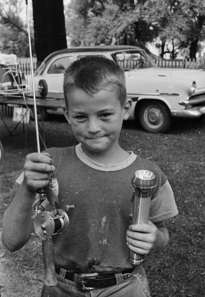 Gary McKenna holds a fishing rod and small fish in one hand and a flashlight in the other. The boy won the flashlight as a prize for being the first to catch a fish in a fishing derby at Tenney Park.