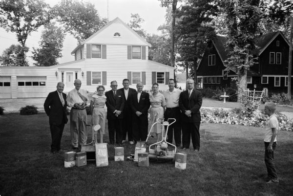 Winners of the 1959 Greater Madison Lawn contest and contest officials standing on the first-prize winning lawn at 2416 Waunona Way, with prizes displayed in front of them. Left to right are: Merle Betts, representing Wolff Kubly and Hirsig; Melvin and Iola Reppen, second place winners; M.E. Moore, third place winner; Perry Offerdahl, general chairman; Arnold Wake, president of the Madison Board of Realtors; James and Charlotte Keffery, first place winners; and Edward Leslie, vice-president of Anchor Savings and Loan. A young boy is standing on the right.