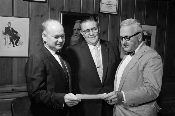 Madison Board of Realtors president Arnold O. Wake, left, presents a check for the Empty Stocking Fund to <i>Wisconsin State Journal</i> editor Roy L. Matson, right. Looking on is Perry E. Offerdahl of the Madison Board of Realtors.