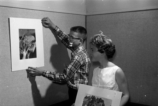 Lloyd Zimmerman hangs one of his pictures as part of a display at the Madison Public Library featuring the artwork of thirteen pupils in the Irene Buck Summer Scholarship program. Eileen Slattery stands at right, ready to put up her own picture.