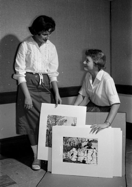 Edith Johnson, left, and June Anderson preparing to hang their pictures as part of a display at the Madison Public Library, featuring the artwork of thirteen pupils in the Irene Buck Summer Scholarship program.