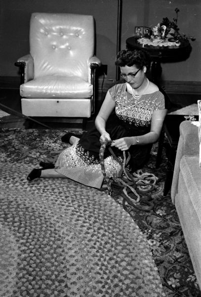 Mary Paulick sitting on the floor while working on a large braided rug.