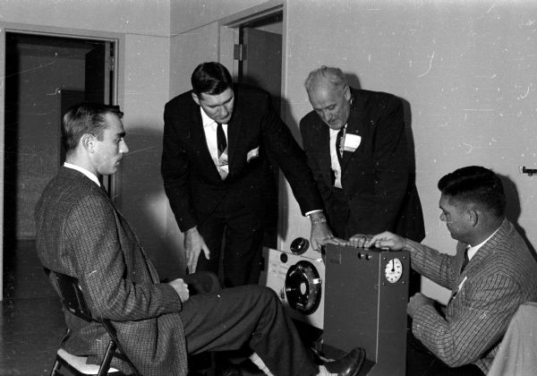 Four men examine a foot operated machine that will measure braking response time of driver education students. The four men are educators and are attending a driver education conference at the University of Wisconsin. Their names are, left to right: David Genzmer, Francis Eckerman, B.A. Precourt, and Dr. Frazier Damron.