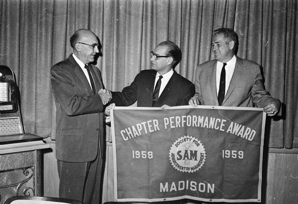 Raymond H. Hansen, center, former president of the Madison chapter of the Society for the Advancement of Management (SAM), receiving an individual award for outstanding service to the organization. At left is C.T. Metz, and right, John S. Lary. Also shown is a banner depicting the local chapter performance award for being one of the top ten chapters in the nation.