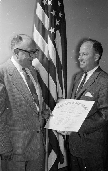 Acting Postmaster for Madison, John F. Whitmore (right), receives a certificate of appointment from Adolph Knudson (left), postal department field services officer, Milwaukee. Whitmore assumed the duties of acting postmaster on September 8, 1958.