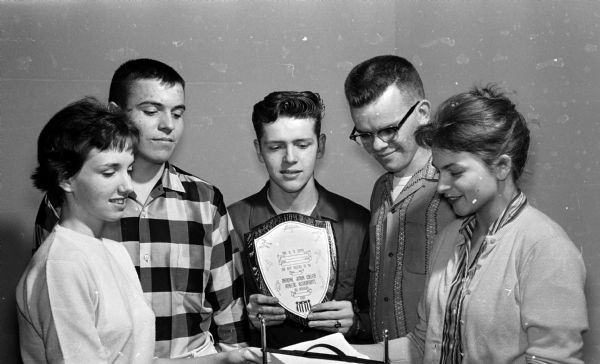 Five members of a Junior Achievement group made up of representatives of the four Madison High Schools accept a plaque for best research in developing new or improved products. Left to right: Ellen Todd, East High; Mark Hoover, Wisconsin High; John Ahrens, East High; Russ Meyer, Central High; and Caroline Marek, West High. Also shown is a sample of their napkin holder product.
