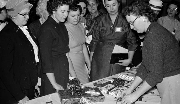 Members of Dane County's 83 Homemakers clubs are taught gift wrapping ideas at their annual Christmas tea. Bernadine Sherwood (right) demonstrates ribbon poinsettias. Looking on from left to right are Mrs. Raymond Lee (Cross Plains), Mrs. Nels Goderstad, Mrs. Kenneth Ripple, and Mrs. Norman Haugen (all of Black Earth).