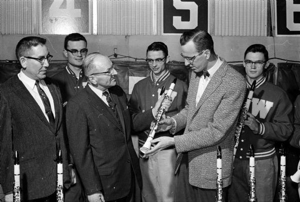 Professor Ray Dvorak, director of university bands, receives a white clarinet from Boris Josheff, president of the Josheff Music Store, Inc. His store is the distributor for the LeBlanc Corporation of Kenosha that gave twenty-three of the rare instruments to the band for use at the Rose Bowl. At left is Kenneth Nester, secretary of the music store. In back are three members of the band's clarinet section, left to right, Max Ellis, Robert Klassy, and David Craig.