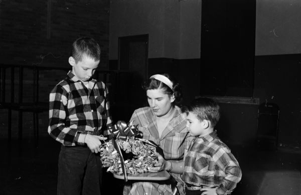 Mrs. Betty Warber puts the finishing touches on a bonbon wreath which will be displayed at the Christmas workshop of the women of St. John's Lutheran Church. The wreath is made of candles, with individual pieces to be cut off and given to children visiting during the holidays. Looking on are Anthony Schumacher (left) and Betty's son, Michael.