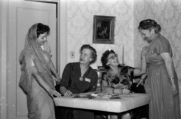 Mrs. Elizabeth A. Risser (left) chatting with her husband's mother, Mrs. Elizabeth W. Risser. Elizabeth is one of the Margaret Rupp Cooper harpists who provided background music at the Red Cross Volunteer "thank you" tea held at the home of the University of Wisconsin president. Mrs. Lucy Haspell, motor service chairman, assists with Mrs. Katherine Grady's name tag.