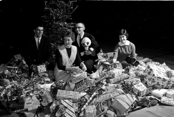 Members of Madison Edgewood High School collect Christmas presents for children of migrant laborers at Endeavor in central Wisconsin. Students brought presents to school, wrapped them, and placed them under the school's Christmas tree. Shown (left to right) are: Thomas Brophy, Mary Miller, Michael Burke, and Mary Kay Ahearn.