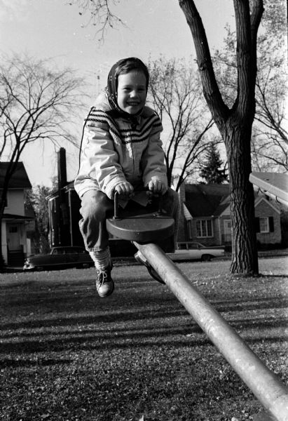 Susan Thomsen smiling from high atop a seesaw on a warm October day while playing at Yahara Place Park near her home at 502 Dunning Street. Houses in the background are 1818 Yahara Place and 1824 Yahara Place.