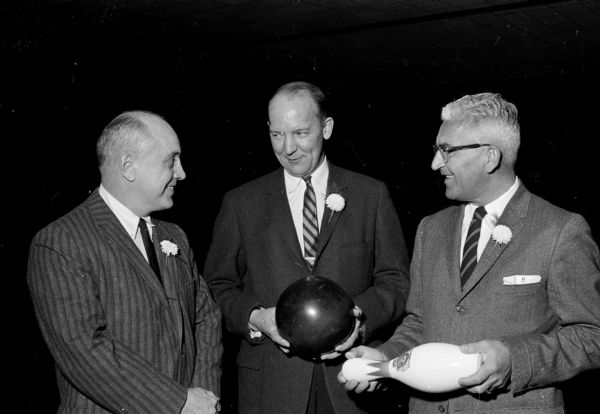 Mayor Ivan Nestingen (center) posing with a bowling ball in his hands before throwing a strike while throwing out the first ball. On the left is Pat Lynaugh, Master of Ceremonies. On the right is Irving Maurer, honorary tournament president.