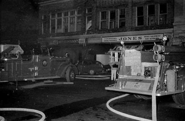 View of Wehrmann's Travel Shop storefront at 508 State Street with a fire truck parked outside. The shop was destroyed by fire late Sunday night. The University of Wisconsin Music School on the second floor and the Jones Typewriter and Business Furniture Company next door were also heavily damaged. Meuer Art Co. located in the building next door had slight smoke damage.