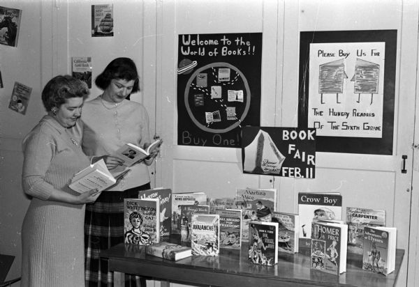 Two parents preview books to be sold to stock the Blessed Sacrament Catholic School library. Joy Genter (left) and Dorothy Clark consider which books to buy and donate to the school library. Posters in background that advertise the event were made in school by the children.