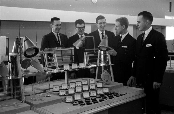 The management staff of the new J.C. Penney Company department store gather around specially designed "cool" spotlights for jewelry counters. Left to right are: James Moe, manager of men's, boys', shoes and work clothes; Palmer Brost, manager of home furnishings, housewares and yard goods; Robert Rystad, manager of women's, girls', infants' and maternity departments; Herschel Martin, assistant manager in charge of sales and merchandise and Robert Mumert, store manager. The store opened March 24 at the Westgate Shopping Center.