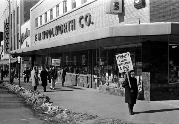 Picketers walk the sidewalk in front of the F.W. Woolworth store on the Capitol Square. The protest was against the company's segregated lunch counter policies in the South.