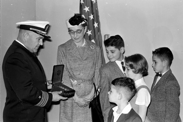 Kathleen Rueber and her four children receive the special medal awarded to her late husband, Gerhardt, for his service. Presenting the medal to Kathleen Rueber is Capt. Reginald Rutherford. The Rueber children are shown at left: Tom, 5; Eileen, 9; Jack, ll; and Bill, 13.