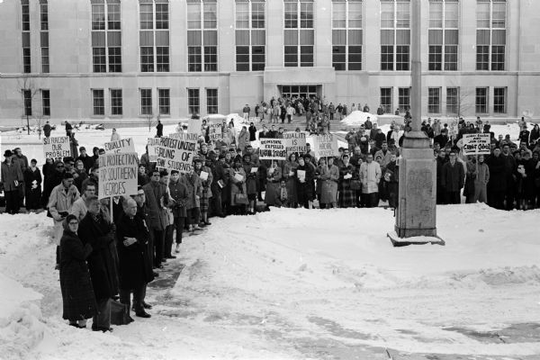 A crowd of five hundred University of Wisconsin students, some carrying protest signs, attend a rally on Library Mall. They are demonstrating peacefully against Southern racial violence regarding a riot in Nashville, Tennessee.