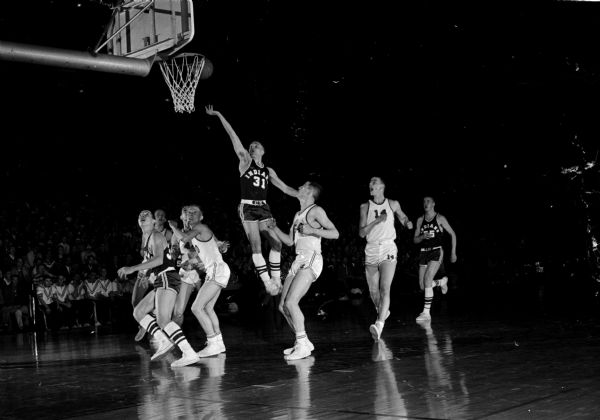 Wayne Sabatke of Menomonie takes a layup shot, rising above the Watertown players during Thursday night of the 1960 State Basketball tournament. Menomonie won over Watertown 66 to 49.
