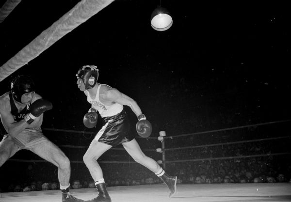 San Jose State's Garvin Kelly is doubled over and covering himself with both hands as Bob Christopherson of the University of Wisconsin swings a looping left. This light heavyweight fight is the only one that did not go the limit.