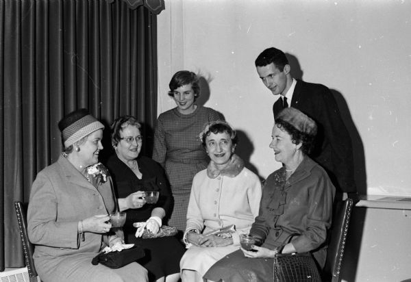 An open house for representatives of University of Wisconsin campus groups, housemothers, and alumni is held at the new Alpha Delta Phi fraternity house. Shown sitting (left to right) are: housemothers Mrs. D.M. Matheson, Kappa Sigma; Mrs. E.T. Link, Alpha Phi; Mrs. Harry E. Consigny, Delta Tau Delta; and Mrs. Esther Heezen, Delta Gamma. Shown standing are (L-R) Dagny Quisling, Madison, WI, Kappa Kappa Gamma; and Richard Germershausen, West Allis, WI, Alpha Delta Phi.