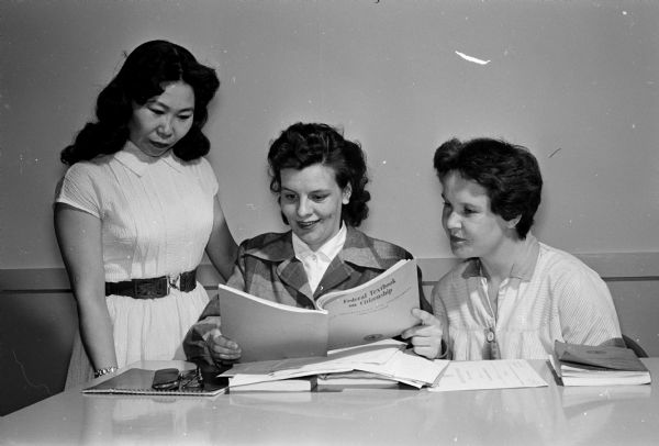 Wives of three airman based at Truax Field participate in an American citizenship course offered by the Truax Field Education Center. Left to right: Shie Barreson, Japan; June Olson, Wales; and Lena Henry, England. They are looking at one of the books used in the course entitled "Federal Textbook on Citizenship."