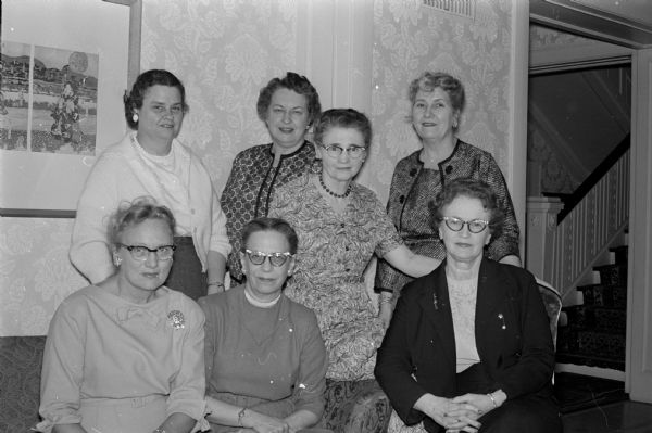 Members attend a house party for officers and board members of the Wisconsin chapter of the PEO Sisterhood (Philanthropic Educational Organization). Hostess and PEO president Constance Elvehjem, standing center, is shown with the other officers. Front row: Mrs. H. Vincent (Milwaukee), Mrs. E.H. Kleispell? (River Falls), Mrs. E.W. Hood (Waukesha), and Dorothy Branham (Rice Lake). Standing at the back are Mrs. R. Hubbell (Wauwatosa), Constance Elvehjem, and Mrs. D.W. Mitchell (Superior).