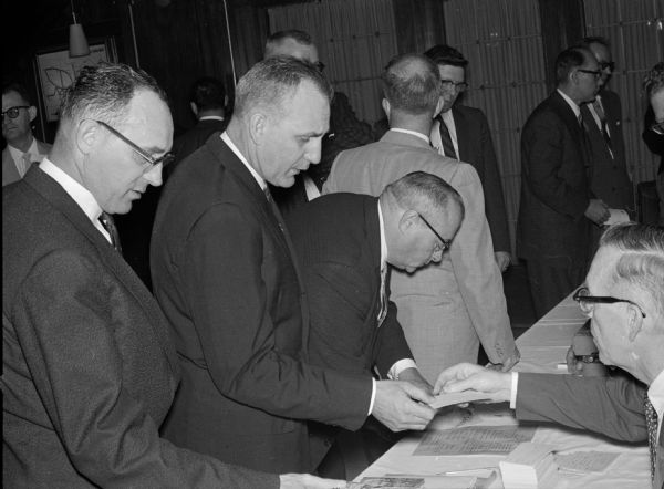 Members of Toastmasters International District 35 register for the 1960 spring conference. Seated at right is Dan Wilkinson, taking registrations. Standing left to right are William Schiller of Milwaukee, and Irv Hundertmerk and C.W. Foster, both of Fond du Lac.