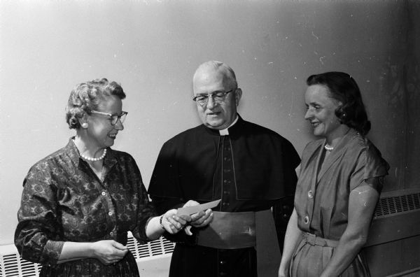 Two members of the Queen's guild of Our Lady Queen of Peace Catholic parish present a check to the pastor, Msgr. F.L. McDonnell. At left is Frances Weller, outgoing president of the guild and at right, Helen Oakland, the guild's new president.
