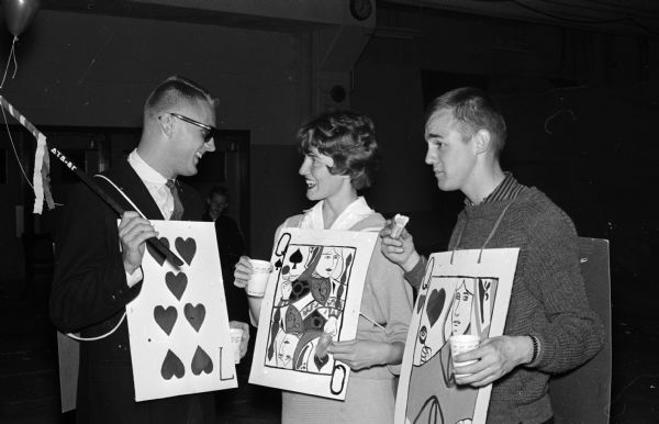 Portrait of three University of Wisconsin students who performed in one of the booths at the U.W. Campus Carnival. They include, from left to right: Neil Brunner, Susie Kamm, and Andy Paulson (each holding a large playing card). The carnival was presented by Pi Beta Phi sorority and Kappa Sigma fraternity with proceeds to be donated to charity.