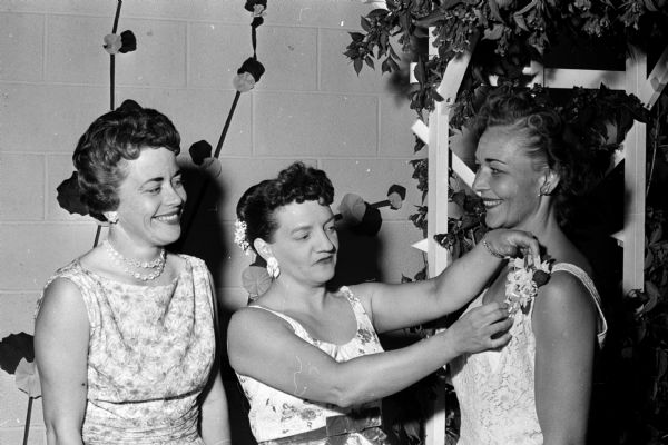 Each guest at the East Side Women's Club's spring banquet is presented with a corsage of spring flowers. Pearl Ludwig (center) pins a corsage on Bernice Zivney as June Hanson looks on.