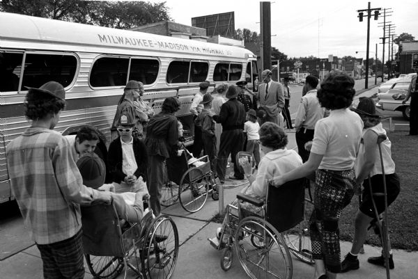 Madison firemen from Station No. 3 and their wives took 32 handicapped children to the Braves-Los Angeles baseball game in Milwaukee. Mayor Ivan Nestigen and Fire Chief Edward J. Page stand by the bus entrance as the firemen's wives push the wheelchairs toward the bus. Station No. 3 is located at 1217 Williamson Street.