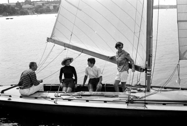 Members of the Mendota Yacht Club plan social arrangements for the 58th annual Inland Lake Yachting Association regatta on Lake Mendota. Social Committee members enjoy a sailboat ride with Reid Saunders (left). Shown from left to right are Mrs. Robert Beck, social committee chairman; Mrs. Austin Faulkner, committee member; and Mrs. Robert Bolz, committee member.