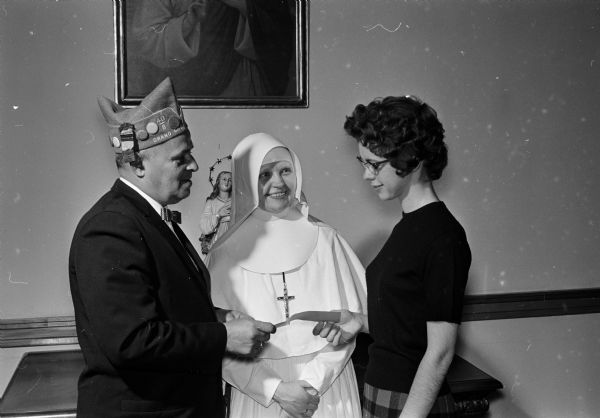 Phyllis Harrington (right) of Arena, a second-year student nurse at St. Mary's, was awarded the Iowa county 40 and 8 chapter nursing scholarship. The presentation was made by Lloyd Richardson (left), third district grand cheminot while wearing a ceremonial hat. Watching at center is Sister M. Suzanne, director of the hospital nursing school. Sister Suzanne is wearing an all white nun's habit.