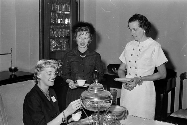 The junior Division of the University of Wisconsin University League hosts a membership tea at the U.W. President's home for newcomers to the U.W. faculty and administrative staff, held at 130 North Prospect Avenue. Shown, left to right, are: Mrs. William Hilsenhoff, 22-C University Houses, and newcomers Mrs. Gene DeFoliart and Mrs. Julian VanLancker.