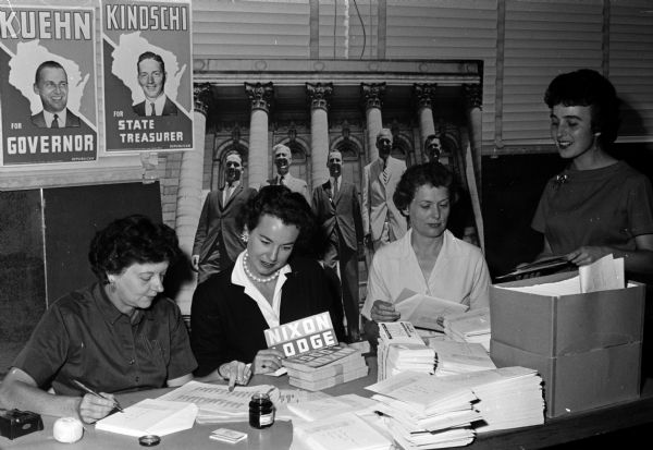 Staff and volunteer workers stuff envelopes at state Republican headquarters. Left to right: Mrs. John Fish and Shirley Jasper (both volunteers); and staff members Selma Shelton and Barbara Barnard. Political material is visible for the campaigns of Kuehn, Kindschi, Nixon, and Lodge.