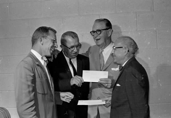 West Side Business Men's Association president W. James Atkins (left) and auction chairman B.E. Miller present checks for money raised at the association's auction to Joseph (Roundy) Coughlin, director of the Fun Fund and William L. Douda of the <i>Wisconsin State Journal</i> representing the Empty Stocking Club.