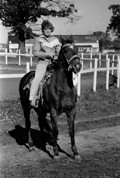 Vickie Stebbins, 16, sitting on her horse, Lady. Seen in the background are buildings and fences at the Bar-M Ranch, near Dane County fairgrounds. Vickie and her horse were featured in a <i>Wisconsin State Journal</i> article by Lousie Marston because Vickie rode her horse along city streets from the ranch to her parent's home on Sherman Avenue, startling Mrs. Stebbins when she saw a horse tethered up near their front door.