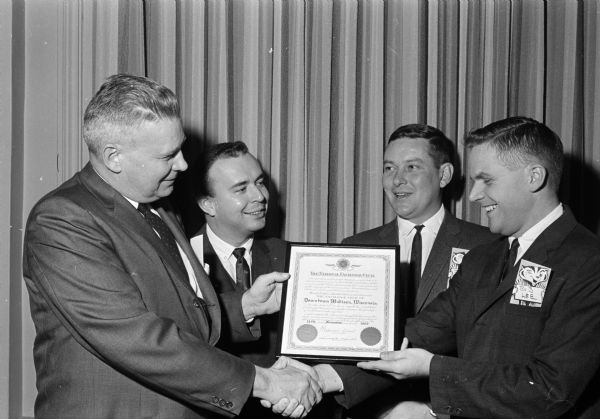 Robert Maurer (left), Milwaukee, presents the charter to Robert Lee, club president, on the extreme left during the chartering ceremony of the Exchange Club of Downtown Madison. In the background is Joe Meagher (left), treasurer, and John D'Orazio, vice president.
