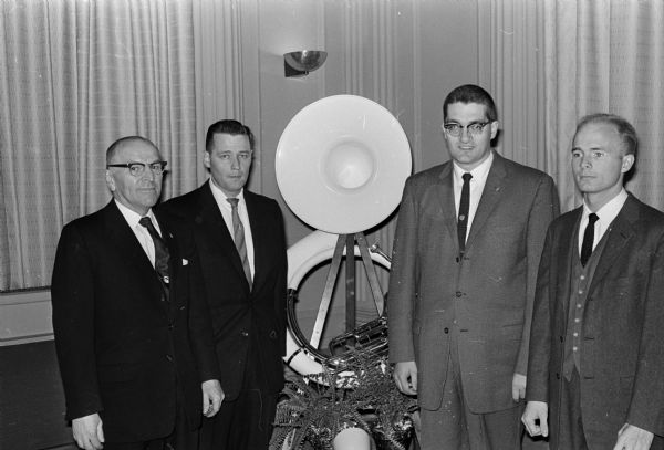 University of Wisconsin marching band officials pose in front of a plastic replica of a tuba at Madison Chamber of Commerce banquet honoring the band. From left are: director Ray Dvorak, co-directors Robert Bittner and Russell Gilligan, and drum major Gerald Stich.