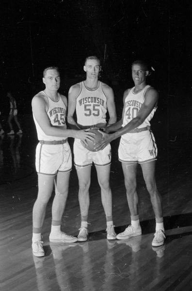Three members of the U.W. basketball team, all very tall and all named Tom, shown standing in uniform with a basketball. These "peeping Toms" are shown left to right: Tom Highbanks, Tom Black, and Tom Gwyn.