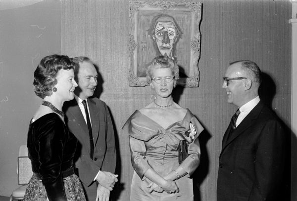 Attendees at "Carnival!," a benefit dinner dance of the Woman's Auxiliary to the Dane County Medical society. In the background are paintings given new identifications for the occasion: names of local doctors. Standing next to a caricature of Dr. Stoops are (left to right) Pauline Burns; Dr. and Mrs. S.H. Ambrose from Whitewater; and Dr. Edward Burns.