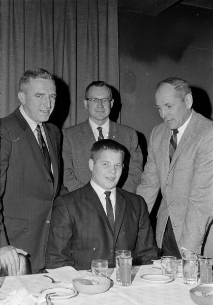 Co-Captain Jim Herrick, sitting, appears to be the center of attraction at the Bank of Madison's annual banquet for Madison Central High school's football team.  Others, left to right, are Harold (Gus) Pollock, Central coach; Jim Warner, toastmaster; and Clark Van Galder, main speaker and assistant coach at U.W. Madison