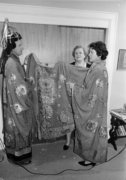 The Three Wise Men in the Christmas pageant at First Methodist Church will wear silk-embroidered robes which came from a Buddhist monastery in China. The robes belong to Eva Brewster who bought them from a curio dealer in Foochow, China where her late husband, Francis Brewster, was an exporter, importer, and banker. Donald Wilkinson, lay leader of First Methodist Church, and Vera Gurland model the robes. The third robe is held by Eva Brewster.