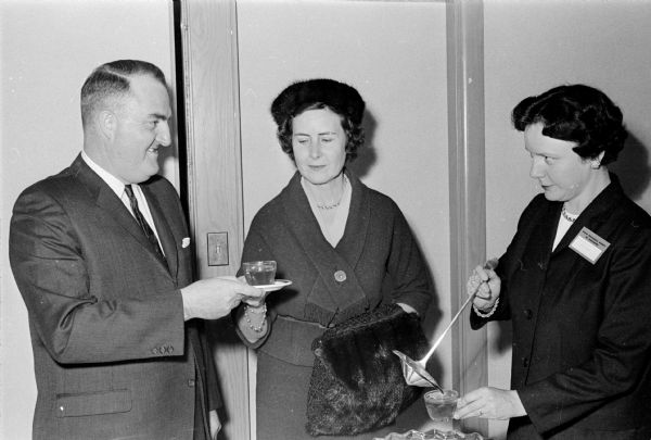 Scott Cutlip, journalism professor at the University of Wisconsin and a member of the board of curators of the State Historical Society, gets a cup of punch at the reception preceding the Society's Founders Day Banquet. Serving him is Arabel Murphy, wife of the Society's president and pouring is Alice Erney, wife of the state archivist.