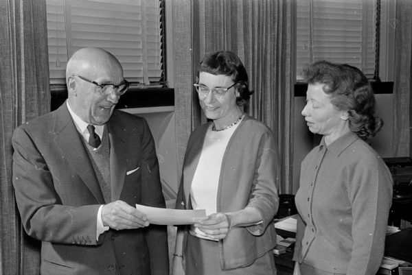 Leo Lunenschloss, left, chairman of the board of the Security State Bank, holds a check for $3,876.71 representing money collected in the 1960 UNICEF drive in Madison. Holding the check with Lunenschloss is Dorothy Daggett, chairman of the 1960 campaign. Frances Rieser, chairman of the 1961 drive is on the right.